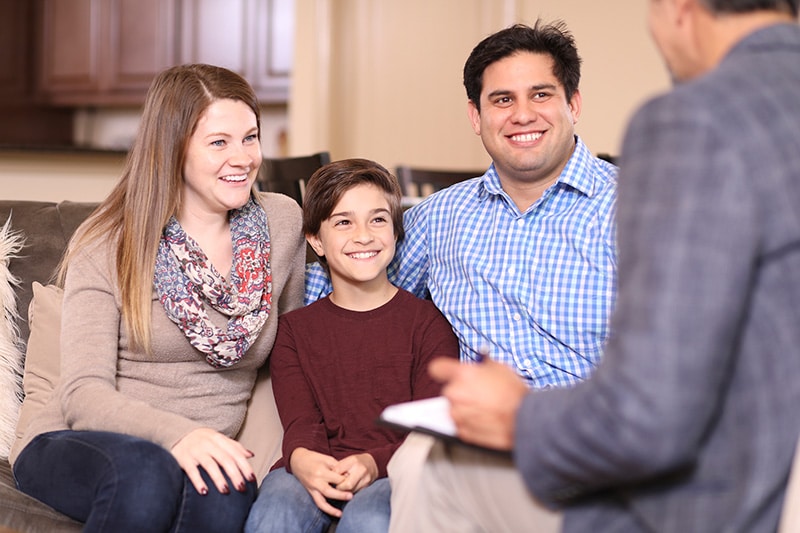 mother and father with their son sitting between them on a sofa during a home visit